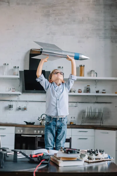 Adorável menino segurando modelo de foguete na cozinha no fim de semana — Fotografia de Stock