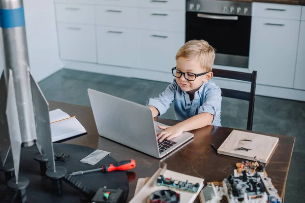 High angle view of boy using laptop at table with rocket model in kitchen on weekend — Stock Photo