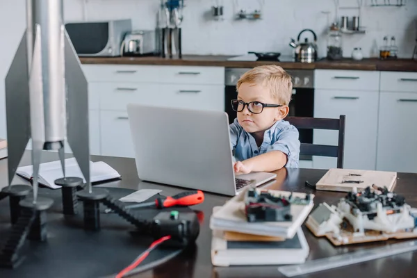 Engraçado adorável menino usando laptop na mesa com modelo de foguete na cozinha no fim de semana — Fotografia de Stock