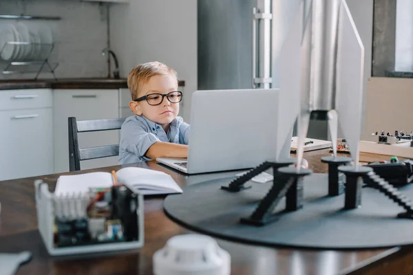 Adorable boy using laptop at table with rocket model in kitchen on weekend — Stock Photo