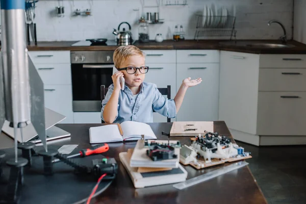 Adorable boy talking by smartphone while modeling rocket in kitchen on weekend — Stock Photo