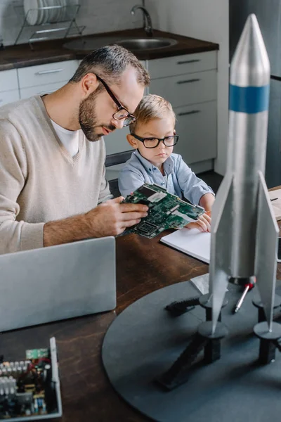 Padre e figlio che riparano insieme il microcircuito, modello a razzo sul tavolo a casa — Foto stock