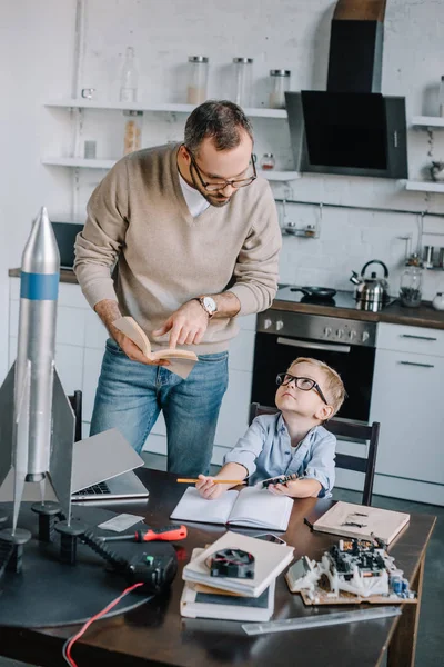 Padre e hijo leyendo literatura para modelar cohetes en casa - foto de stock