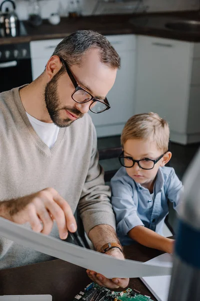 Father and son in glasses modeling rocket and looking at blueprint at home — Stock Photo