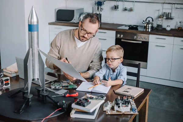 Padre e figlio modellazione razzo e guardando cianografia a tavola in cucina — Stock Photo