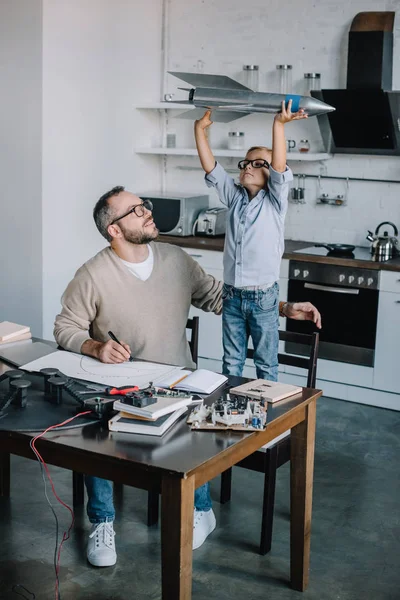 Adorable son holding rocket model at table at home — Stock Photo