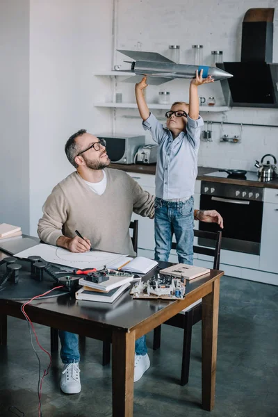 Adorável filho segurando modelo de foguete na mesa em casa — Fotografia de Stock