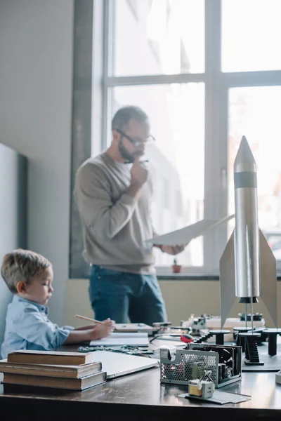 Padre pensativo e hijo modelando cohete en casa - foto de stock