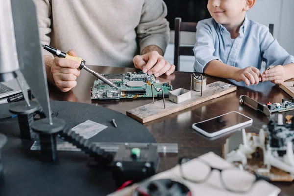 Cropped image of father and son soldering circuit board with soldering iron at home — Stock Photo
