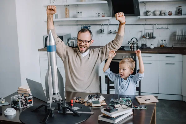 Felice padre e figlio con le mani alzate guardando il modello di razzo a casa — Foto stock