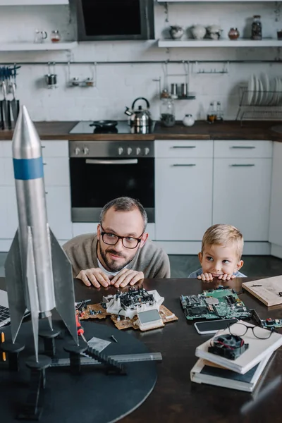 Pai e filho olhando para fora da mesa na cozinha e olhando para o modelo de foguete — Fotografia de Stock