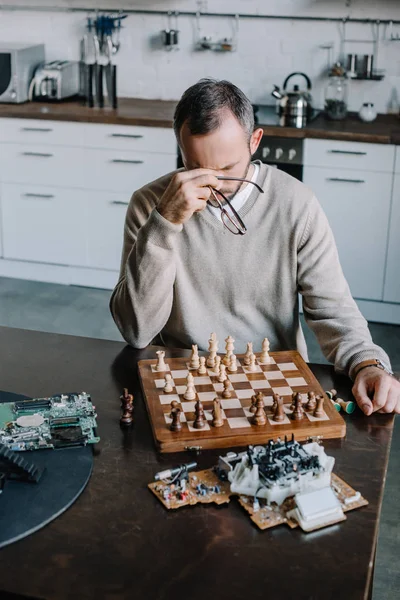 Blick aus der Vogelperspektive auf einen müden Mann, der zu Hause Schach spielt und Nasenrücken berührt — Stockfoto