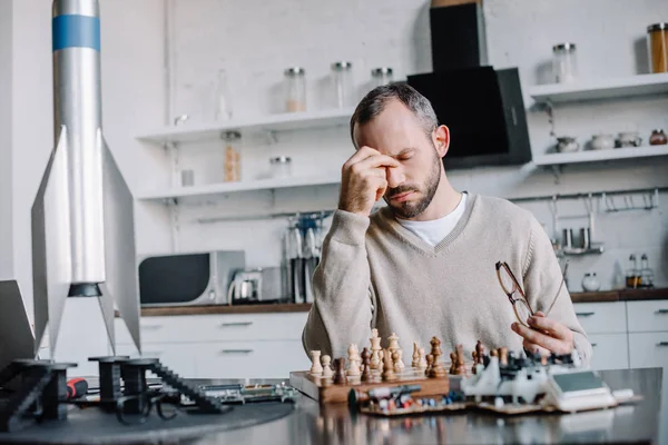 Fatigué bel homme jouant aux échecs et touchant nez pont à la maison — Photo de stock