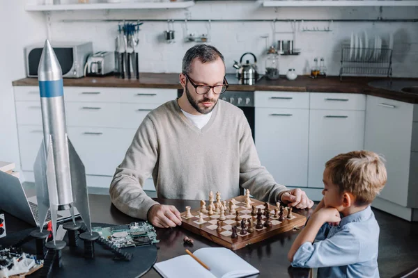 Vista de ángulo alto de padre e hijo pequeño jugando ajedrez juntos en casa - foto de stock