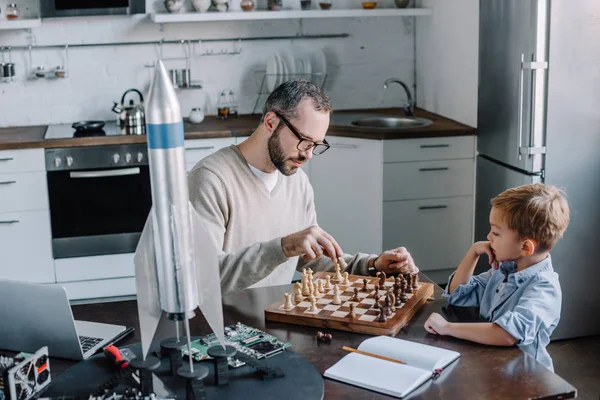 Pai e filho pequeno bonito jogando xadrez juntos em casa — Fotografia de Stock