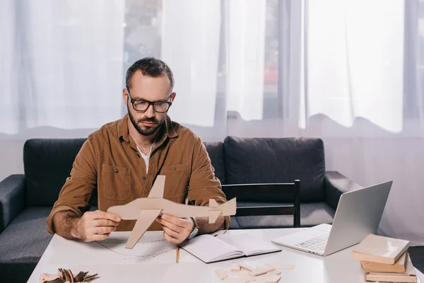 Focused man in eyeglasses holding cardboard plane while modeling at home — Stock Photo