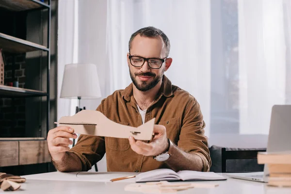 Красивый улыбающийся мужчина в очках, держащий картонный самолет, моделируя дома — стоковое фото