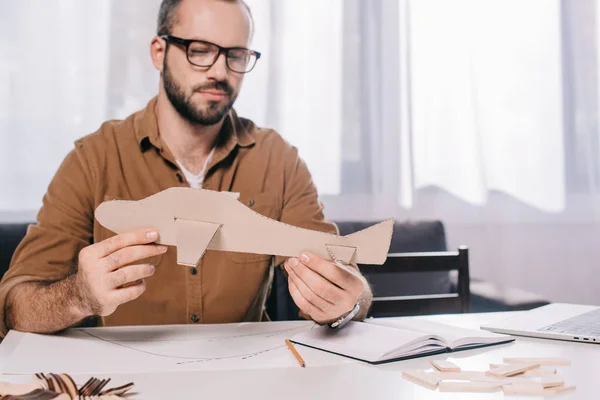 Красивый мужчина в очках, держащий картонный самолет во время моделирования дома — стоковое фото