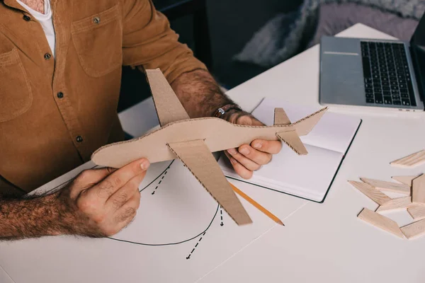 Tiro recortado de homem segurando modelo de avião de papelão enquanto modelagem em casa — Fotografia de Stock