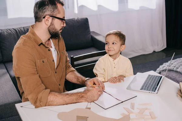 Vater und süßer kleiner Sohn schauen sich beim gemeinsamen Modellfliegen zu Hause an — Stockfoto