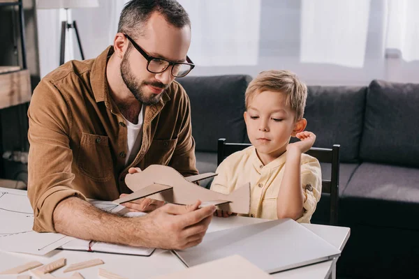 Vater mit Brille und süßer kleiner Sohn modelt gemeinsam Flugzeug zu Hause — Stockfoto