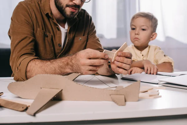 Tiro recortado de pai e filho pequeno modelando avião de brinquedo juntos em casa — Fotografia de Stock