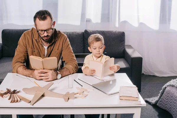 Aus der Vogelperspektive: Vater und kleiner Sohn lesen Bücher, während sie zu Hause ein Flugzeug modellieren — Stockfoto