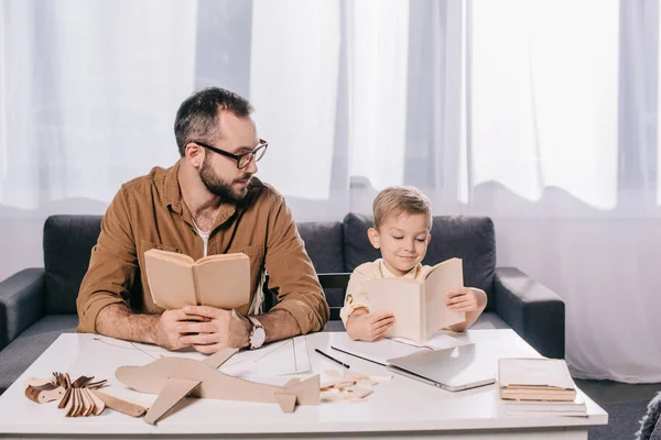 Padre e hijo pequeño sosteniendo libros mientras modelaba avión en casa - foto de stock