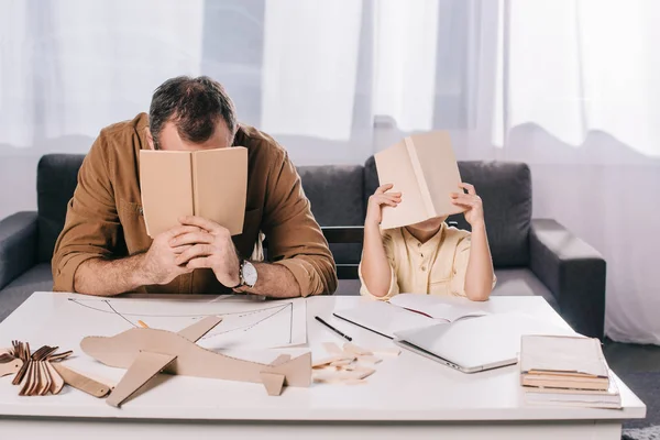 Father and son hiding faces behind books while modeling together at home — Stock Photo