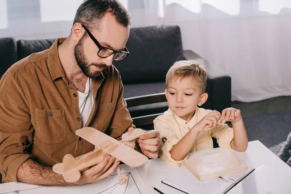 Visão de alto ângulo de pai e filho pequeno modelando avião de brinquedo juntos em casa — Fotografia de Stock