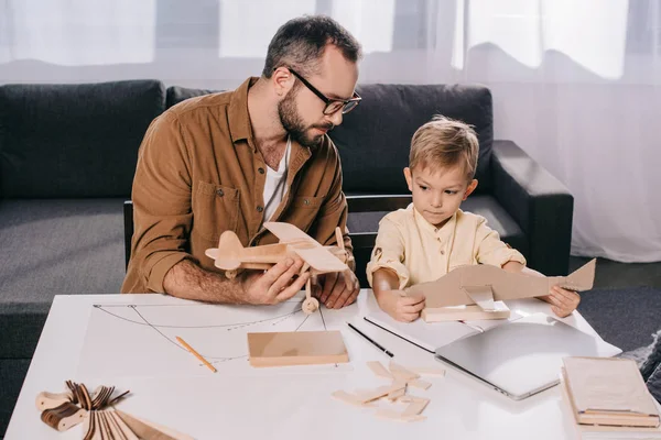 Pai em óculos e bonitinho filho modelando aviões juntos em casa — Fotografia de Stock