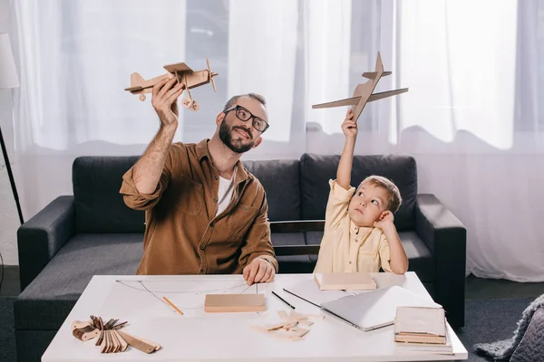 Glücklicher Vater und Sohn halten Spielzeugflugzeuge beim gemeinsamen Modellieren zu Hause — Stockfoto