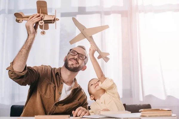 Feliz padre e hijo pequeño jugando con aviones de madera modelos en casa - foto de stock