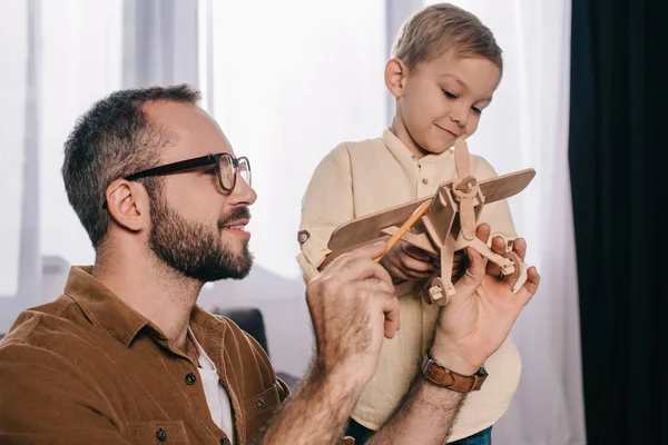 Happy father and son playing with wooden plane model together at home — Stock Photo