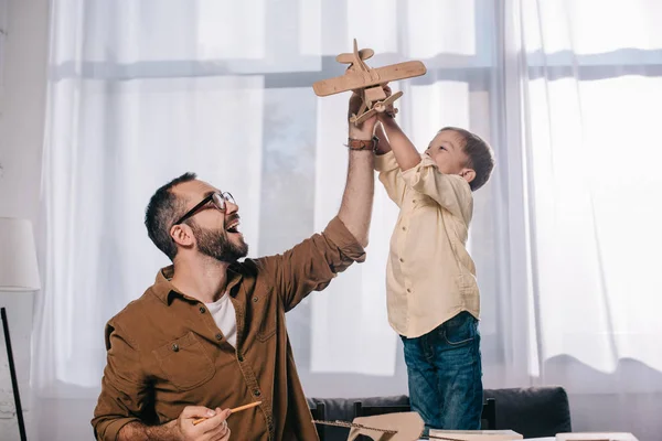 Pai feliz e filho pequeno brincando com avião de brinquedo de madeira enquanto modelando juntos em casa — Fotografia de Stock