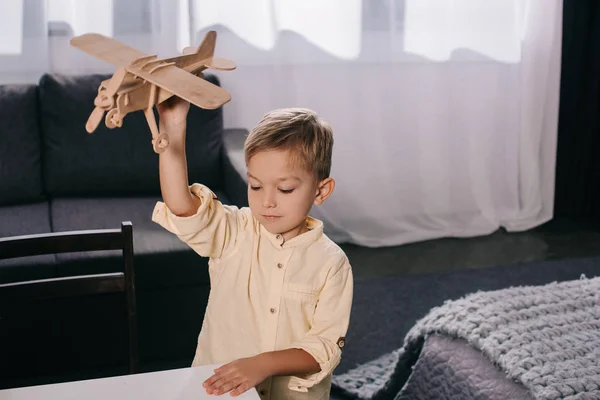 Vista de ángulo alto de adorable niño jugando con el modelo de avión de madera en casa - foto de stock