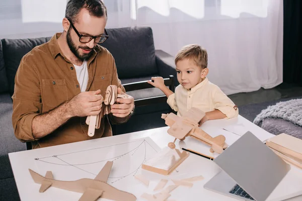 Pai feliz e filho modelar avião de madeira em casa — Fotografia de Stock