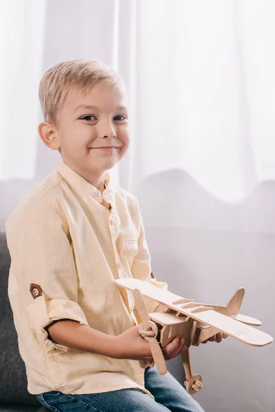 Adorable little boy holding wooden toy plane and smiling at camera — Stock Photo
