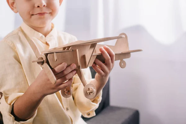 Cropped shot of little boy holding wooden toy plane at home — Stock Photo