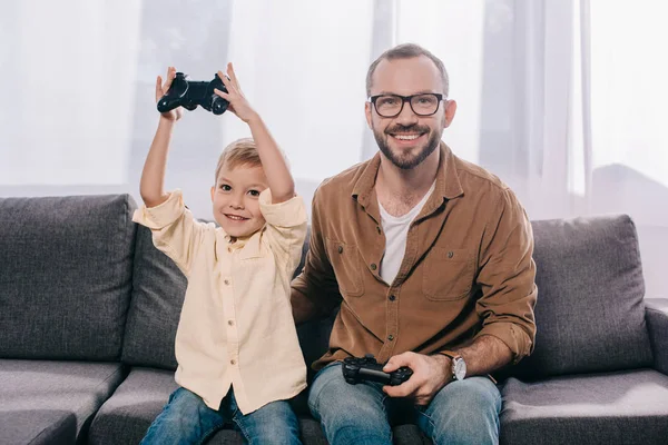 Happy father and son using joysticks and smiling at camera — Stock Photo