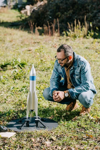 Handsome man in eyeglasses looking at model rocket outdoor — Stock Photo