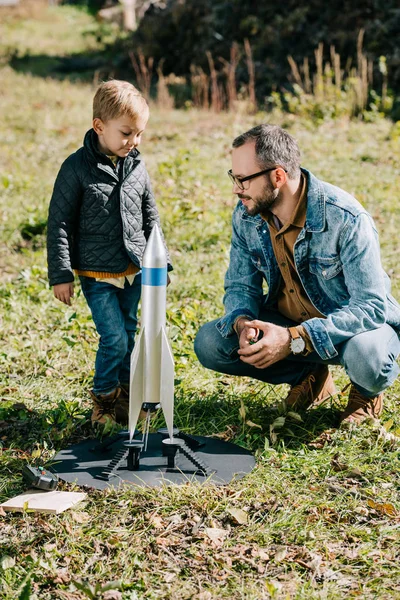 Щасливий батько і милий маленький син грає з моделлю ракети на відкритому повітрі — стокове фото