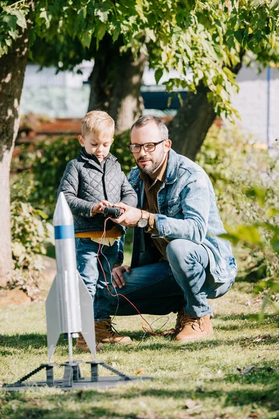 Happy father and son launching model rocket together at sunny day — Stock Photo