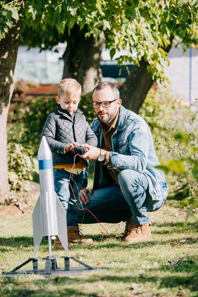 Feliz padre e hijo lanzando cohete modelo juntos en el día soleado - foto de stock