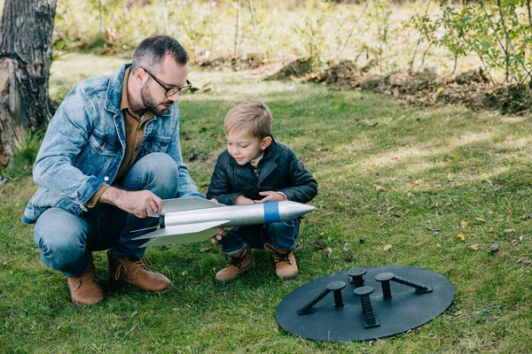 Батько і маленький син грають з моделлю ракети на траві — стокове фото