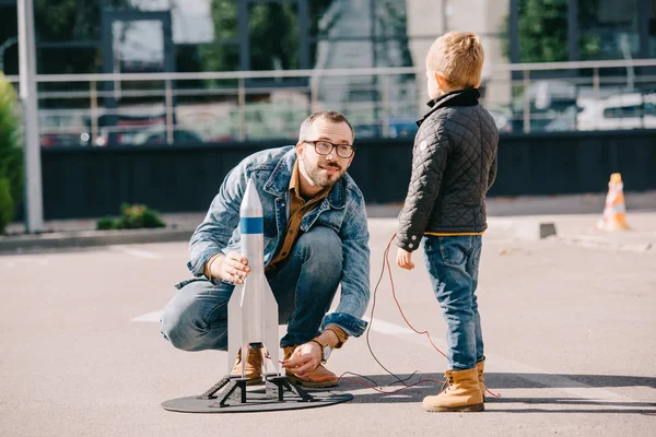 Father and son launching model rocket together outdoor — Stock Photo