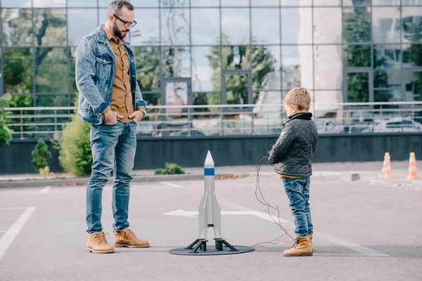 Padre mirando pequeño hijo lanzamiento modelo cohete al aire libre - foto de stock
