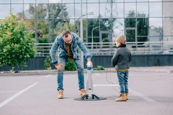 Padre e hijo pequeño jugando con el modelo cohete juntos - foto de stock