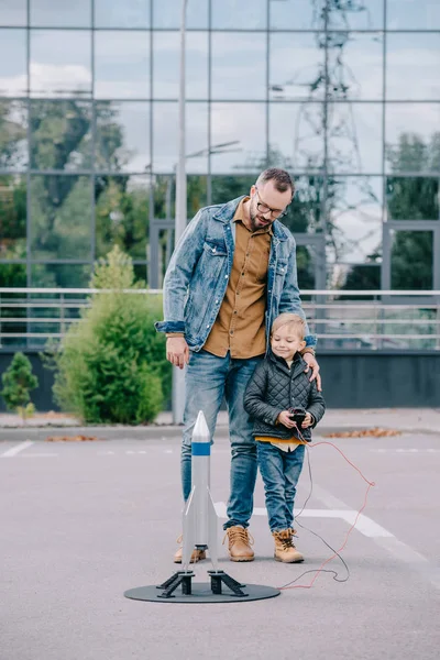 Glücklicher Vater und kleiner Sohn starten Modellrakete im Freien — Stockfoto