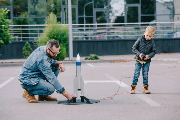Pai e pequeno filho brincando com modelo de foguete ao ar livre — Fotografia de Stock